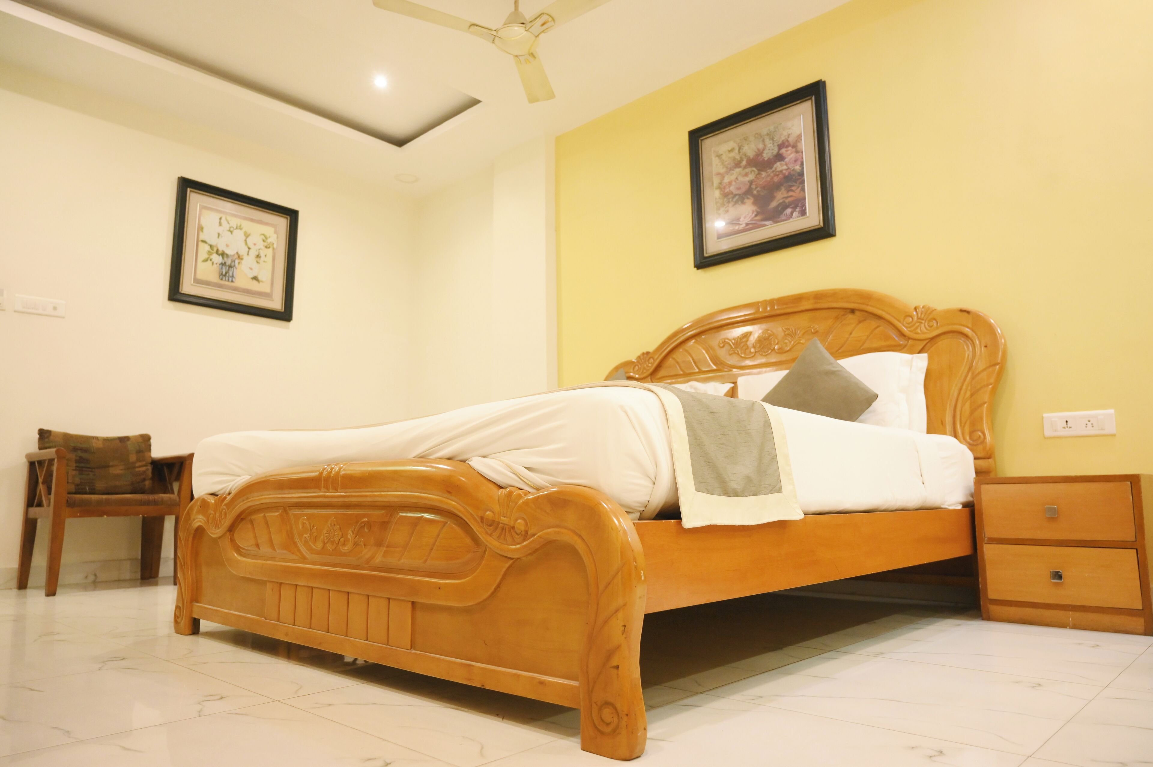 Una cama de madera con cabecera, una mesita de noche y una silla en una habitación con paredes amarillas y un ventilador de techo.
