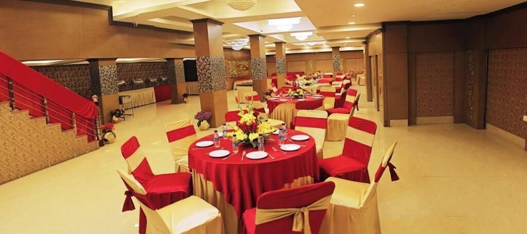 A banquet hall with round tables, red and white chairs, and a staircase on the left.