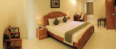 Quarto de hotel com uma cama grande, mesas de cabeceira, uma escrivaninha e uma cadeira.