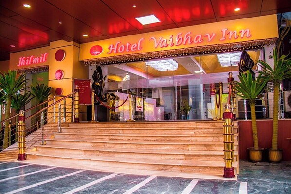 Hotel Vaibhav Inn con una escalera de mármol que conduce a la entrada, rodeado de plantas en macetas.