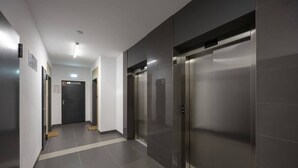 Corredor moderno com dois elevadores, uma porta com um aviso e um luminário no teto.
