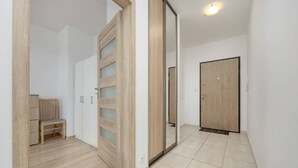 Um corredor com porta de madeira, espelho, um banco e guarda-roupa.