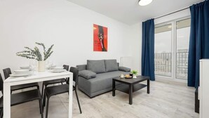 Un salon moderne avec un canapé gris, une table à manger avec des chaises, une petite table basse et une grande fenêtre ornée de rideaux bleus.