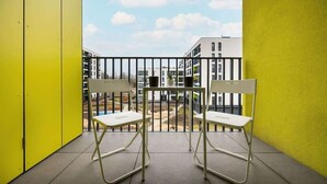 Un balcon avec deux chaises et une table, des murs jaunes et une vue sur des immeubles.