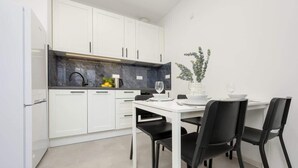 Une cuisine moderne avec des meubles blancs, un plan de travail noir et un coin repas comprenant une table blanche et des chaises noires.