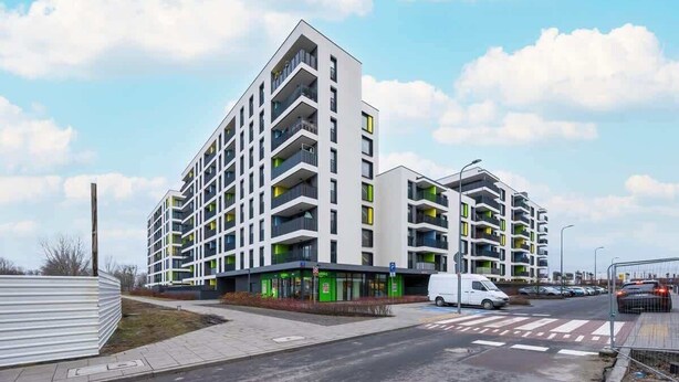 Un immeuble résidentiel moderne à plusieurs étages, doté de balcons, d’un espace de stationnement et d’un passage piéton.