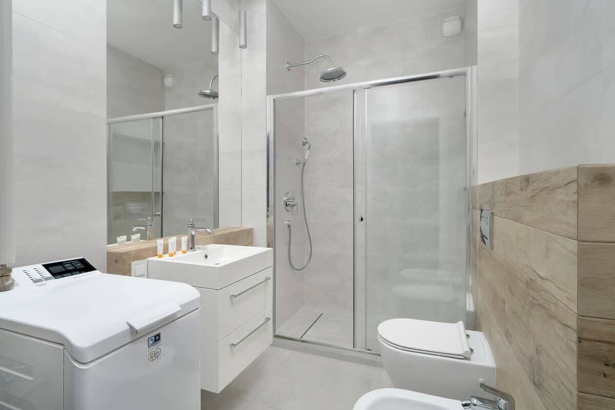 Ein modernes Badezimmer mit einer gläsernen Duschkabine, einem weißen Waschbecken und einer Toilette.