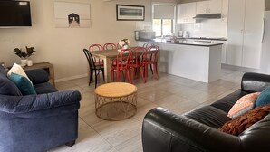 Una cocina moderna con armarios blancos, una zona de comedor con sillas rojas y un sofá de cuero negro.
