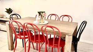 Un comedor con una mesa de madera y sillas rojas, una planta pequeña y un cuadro en la pared.