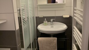 A modern bathroom with a glass shower enclosure, a white sink with a mirror above, and a towel rack.
