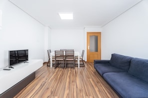 A living room with a flat-screen TV, a dining table with chairs, a sofa, and a wooden door. - Apartment "Ca Vivi" with Private Terrace & Wi-Fi (Catarroja)