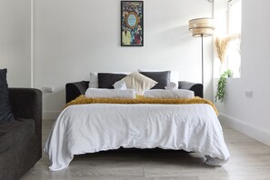 A neatly arranged bedroom with a bed, a sofa, a floor lamp, and a wall-mounted picture. - Urban Heaven - 6 Sleeper in the Heart of Bricklane (London)