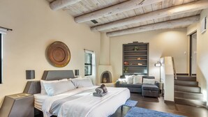 A modern bedroom with a large bed, a desk, and a sofa. There is a window and a staircase in the background. - Experience luxury at Sedona Red Mountain Retreat, a spacious 3-bedroom house with stunning views. (Sedona)