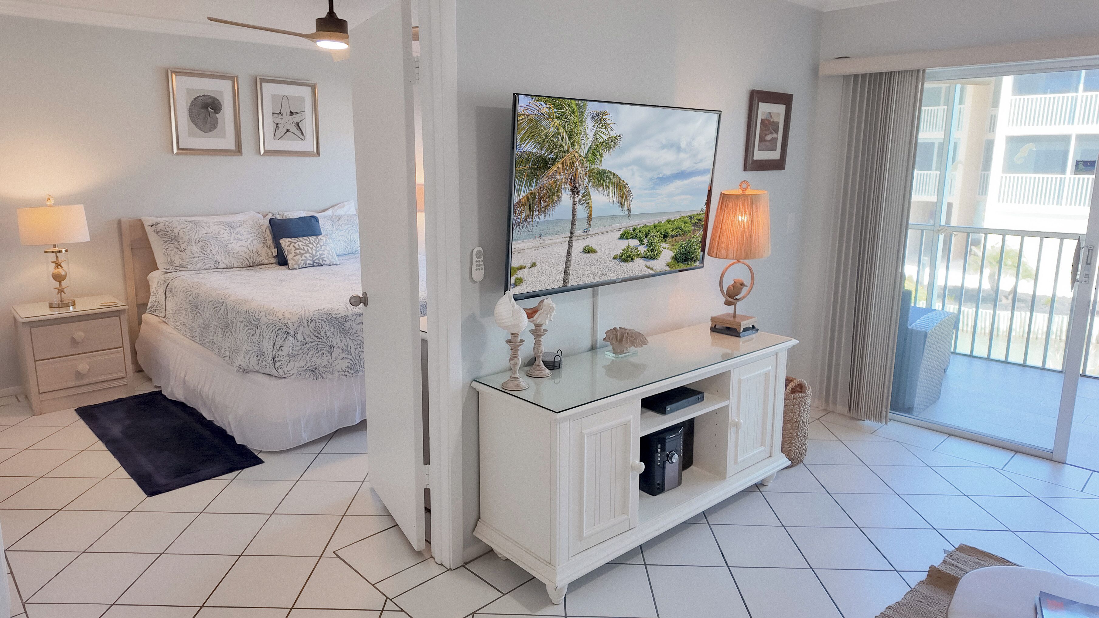 Un dormitorio con cama, mesita de noche, televisor, consola y balcón con vistas.
