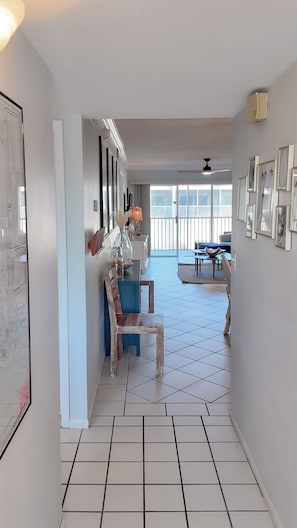 A spacious living area with a dining table and chairs, a blue sofa, and a large window with a view of the outside. - Sandy Feet and Sea Shells Welcome Here (Sanibel)