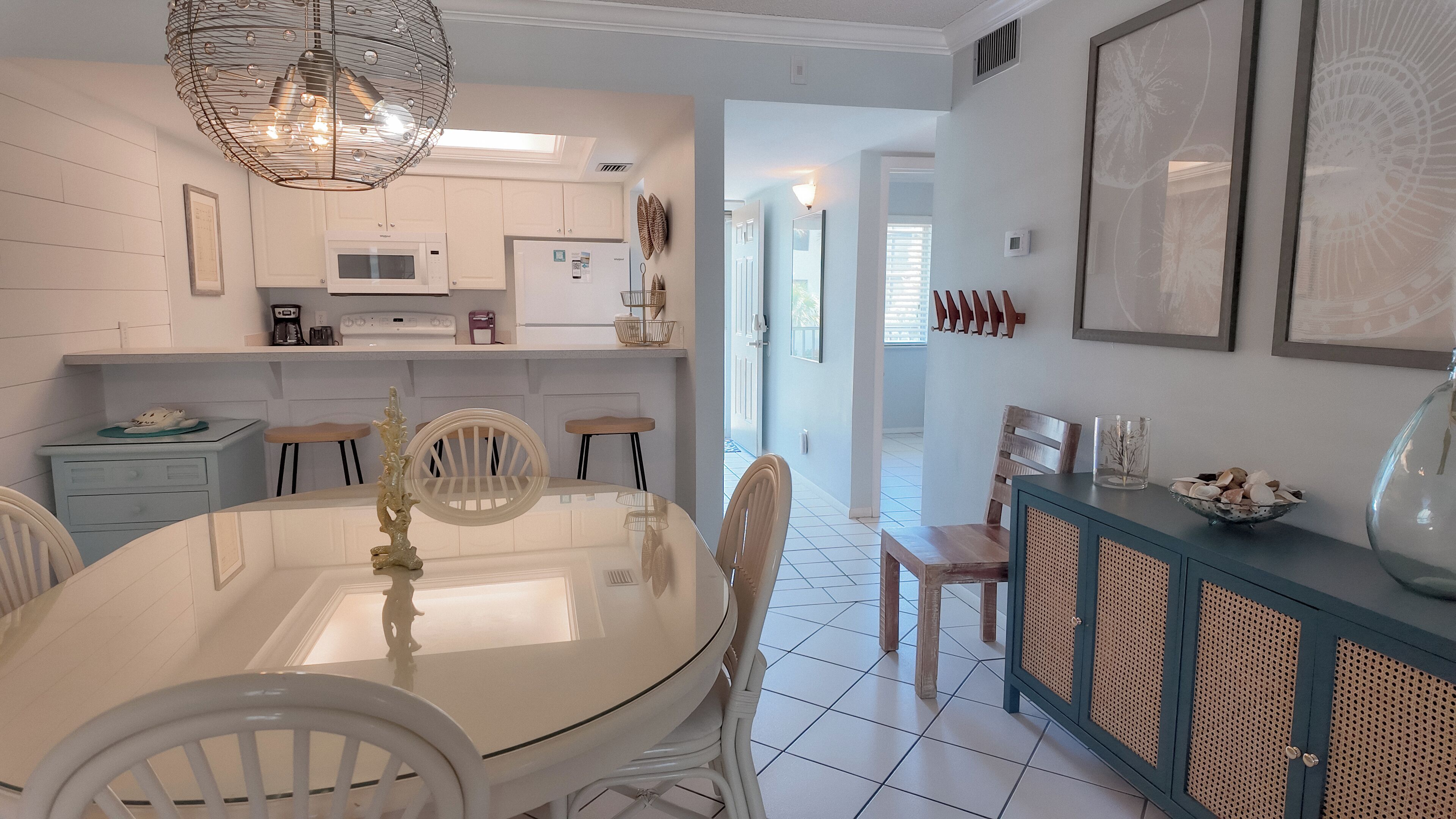 A modern kitchen with white cabinetry, a dining table with chairs, a chandelier, and a view into the adjacent dining area.