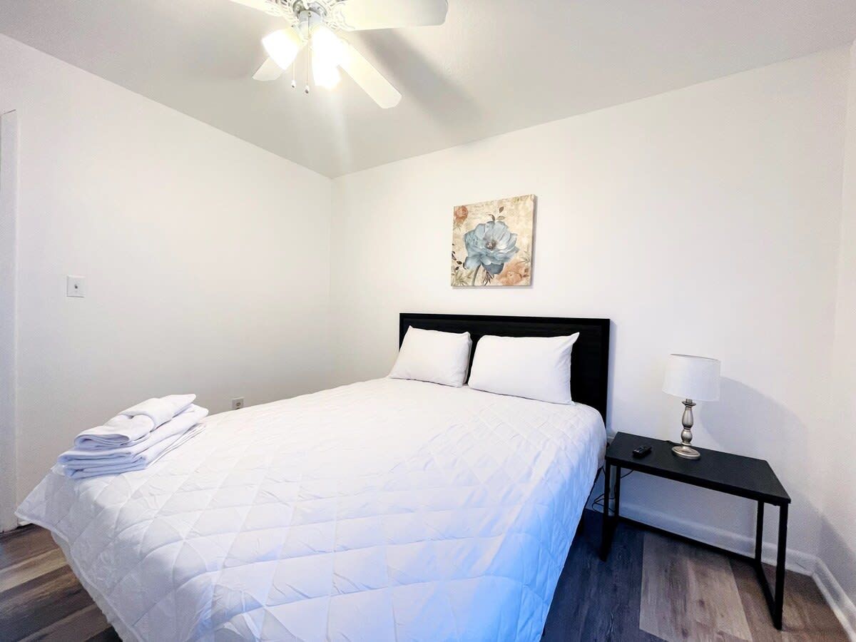 A neatly made bed with white bedding, a black headboard, and a small bedside table with a lamp.