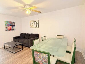 A modern living room with a glass-top dining table, a grey sofa, a ceiling fan, and artwork on the walls. - Beautiful and Tranquil Cherry Grove Beach (North Myrtle Beach)