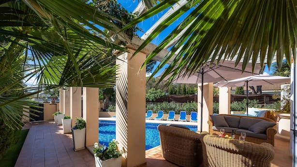 Ein Poolbereich mit Liegestühlen, einer Rattan-Couch und einer Pergola mit Palmen.