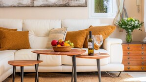 Ein Wohnzimmer mit einem weißen Sofa, einem Couchtisch mit Obstkorb, einer Weinflasche und Gläsern.