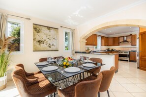 A modern dining area with a glass table set for six, surrounded by brown upholstered chairs.