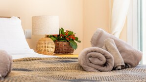 Ein ordentlich bezogenes Bett mit einem zusammengerollten Handtuch, einem Korbwäscher mit roten Blumen und einer Lampe auf einem Nachttisch.