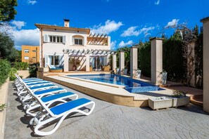 A poolside area with lounge chairs, a swimming pool, and a building with a pergola.
