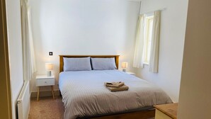 A bedroom with a wooden bed, two bedside tables with lamps, a radiator, and a window with curtains. - Bright Modern Welcoming Home Easy Stroll Along Pathway Into Kenmare Town (Kenmare)
