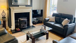 A modern living room with a fireplace, a black leather sofa, a glass coffee table, and a television. - Bright Modern Welcoming Home Easy Stroll Along Pathway Into Kenmare Town (Kenmare)