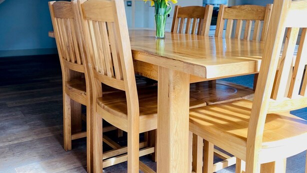 A wooden dining table with six chairs, a vase with yellow flowers, and a kitchen in the background. - Bright Modern Welcoming Home Easy Stroll Along Pathway Into Kenmare Town (Kenmare)