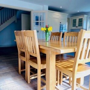 A wooden dining table with six chairs, a vase with yellow flowers, and a kitchen in the background. - Bright Modern Welcoming Home Easy Stroll Along Pathway Into Kenmare Town (Kenmare)