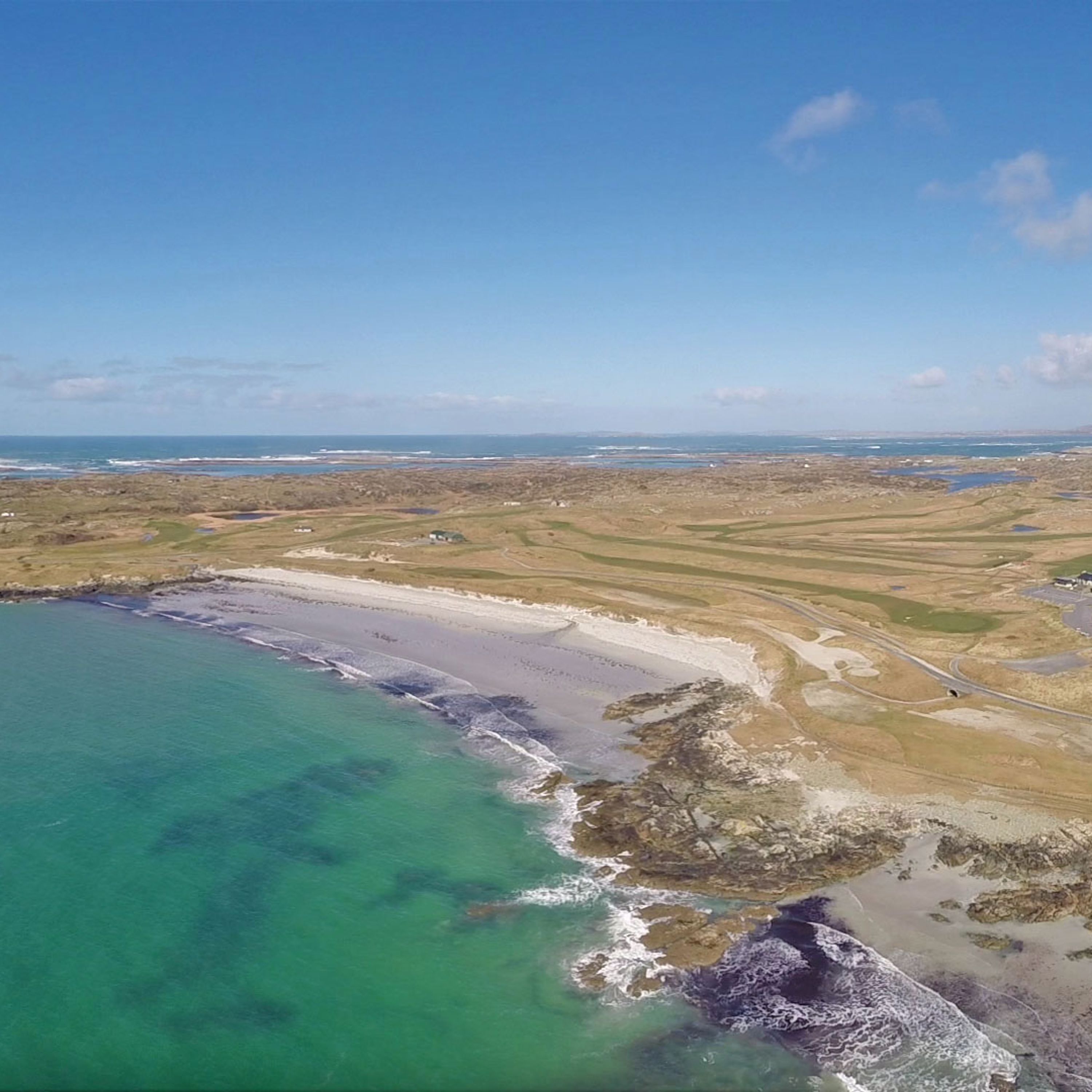An aerial view of a coastal area with clear turquoise waters, sandy beaches, and rolling hills.