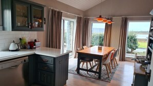 Uma cozinha com armários escuros, bancada branca e um espaço de refeições com mesa e cadeiras de madeira.