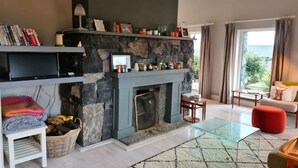 Uma sala de estar com lareira de pedra, televisão de tela plana, sofá e mesa de centro de vidro.