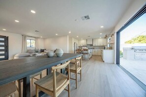A spacious kitchen with a long wooden table and chairs, a dining area with a sofa, and a view of the outdoors through large windows. - Luxury Old Town Scottsdale Home with Pool and Spa (Scottsdale)