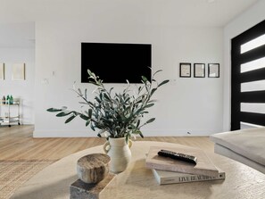 A living room with a modern design, featuring a large black TV mounted on the wall, a potted plant, a remote control, and a couple of books on a wooden table. - Luxury Old Town Scottsdale Home with Pool and Spa (Scottsdale)