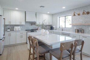A modern kitchen with white cabinets, a central island with chairs, a built-in oven, and a window providing natural light. - Luxury Old Town Scottsdale Home with Pool and Spa (Scottsdale)