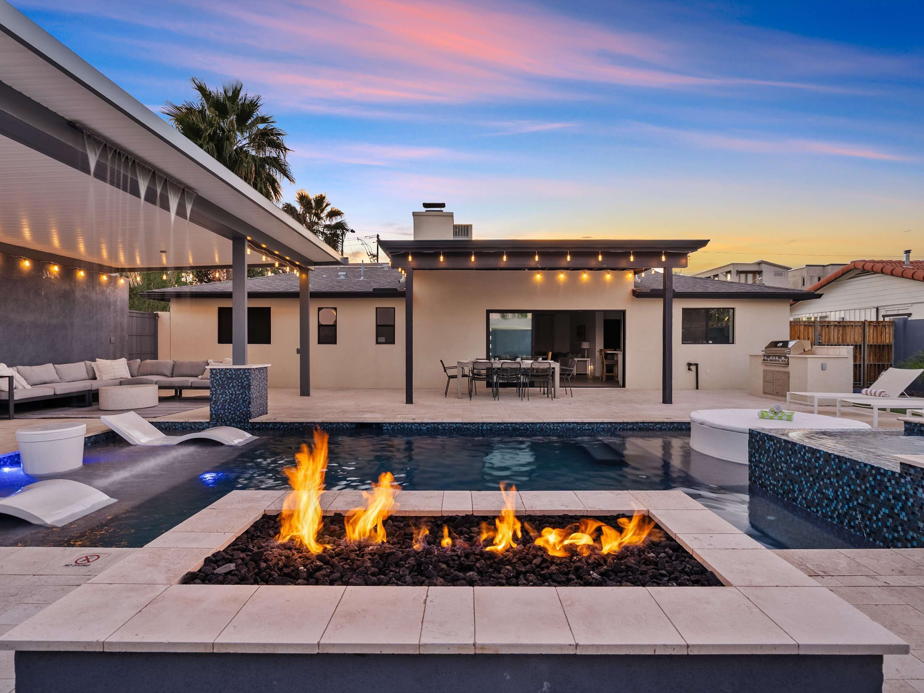 Une terrasse extérieure moderne, dotée d’une piscine, d’un foyer et de mobilier d’extérieur.