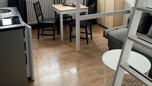 Ein kleines Zimmer mit Etagenbett, Tisch und Stuhl. Es gibt einen Heizkörper und ein Fenster mit Vorhängen.