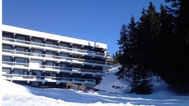 Ein mehrstöckiges Gebäude mit Balkonen, umgeben von Schnee und Bäumen.