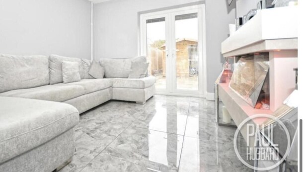 Un salon moderne avec un canapé d’angle gris, une porte vitrée donnant sur l’extérieur et un sol en marbre.
