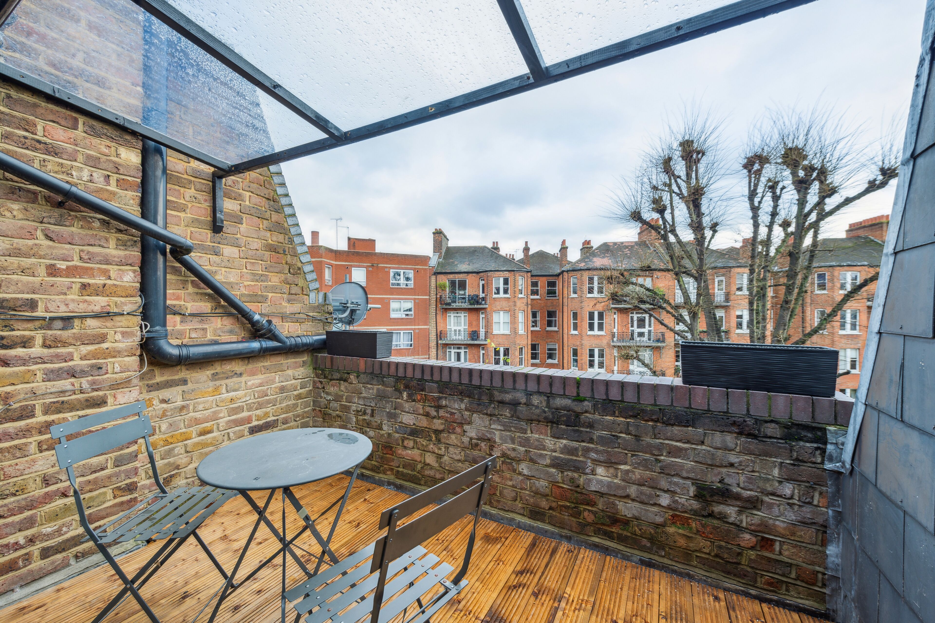 A balcony with a brick wall, a wooden floor, and a table with chairs.