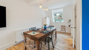 Een eetgedeelte met een houten tafel, transparante stoelen en een vaas met bloemen. Er is een raam met uitzicht op gebouwen.