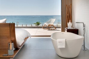 A modern bedroom with a large bed, a freestanding bathtub, and a view of the ocean. - Villa Miramar (Frontignan)