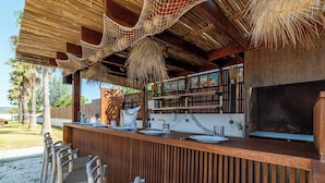 A wooden bar with a thatched roof, outdoor seating, and a view of the ocean. - Villa Miramar (Frontignan)