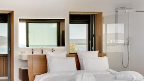 A modern bedroom with a large bed, two bedside tables, a built-in shower, and large windows offering a view of the sea. - Villa Miramar (Frontignan)