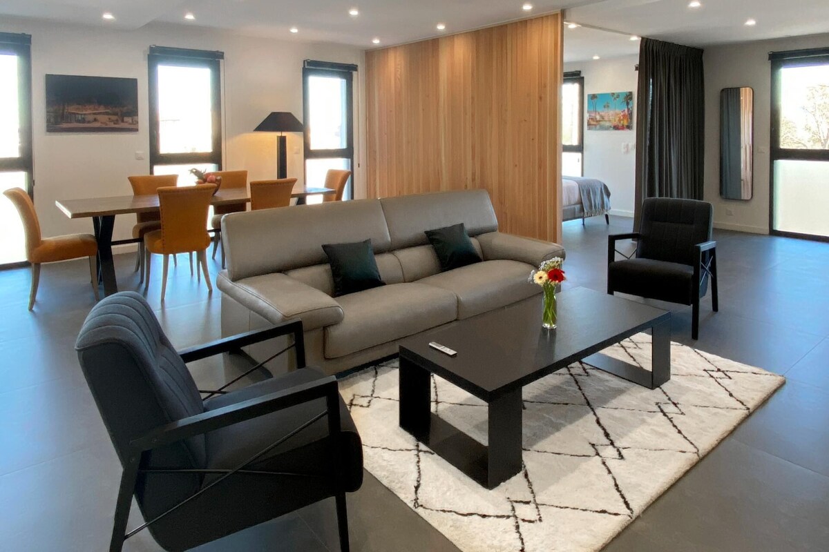 A modern living room with a sofa, armchairs, a coffee table, and a dining area with chairs and a table.
