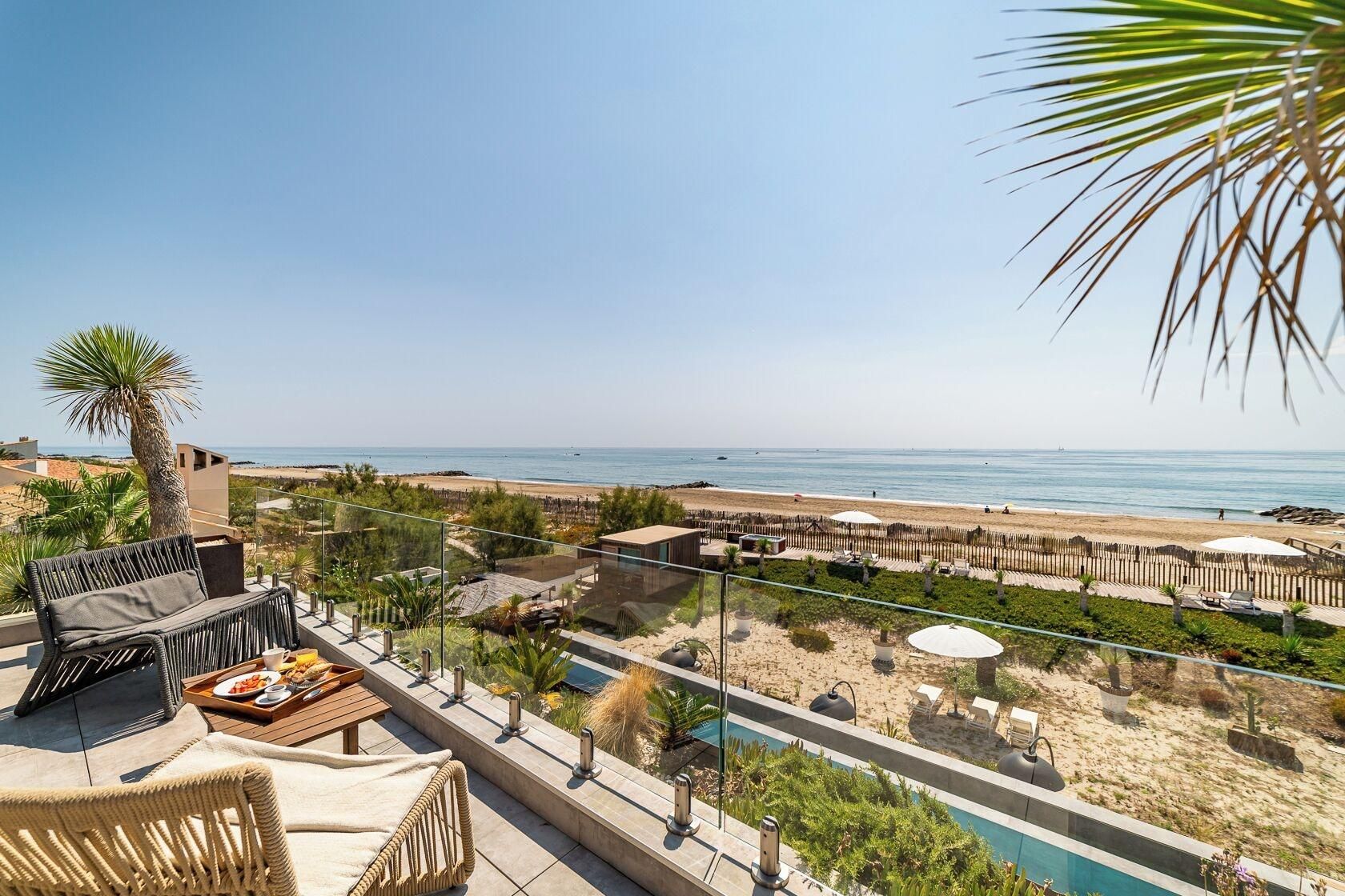 A balcony with a view of the beach, outdoor seating, and a pool area.