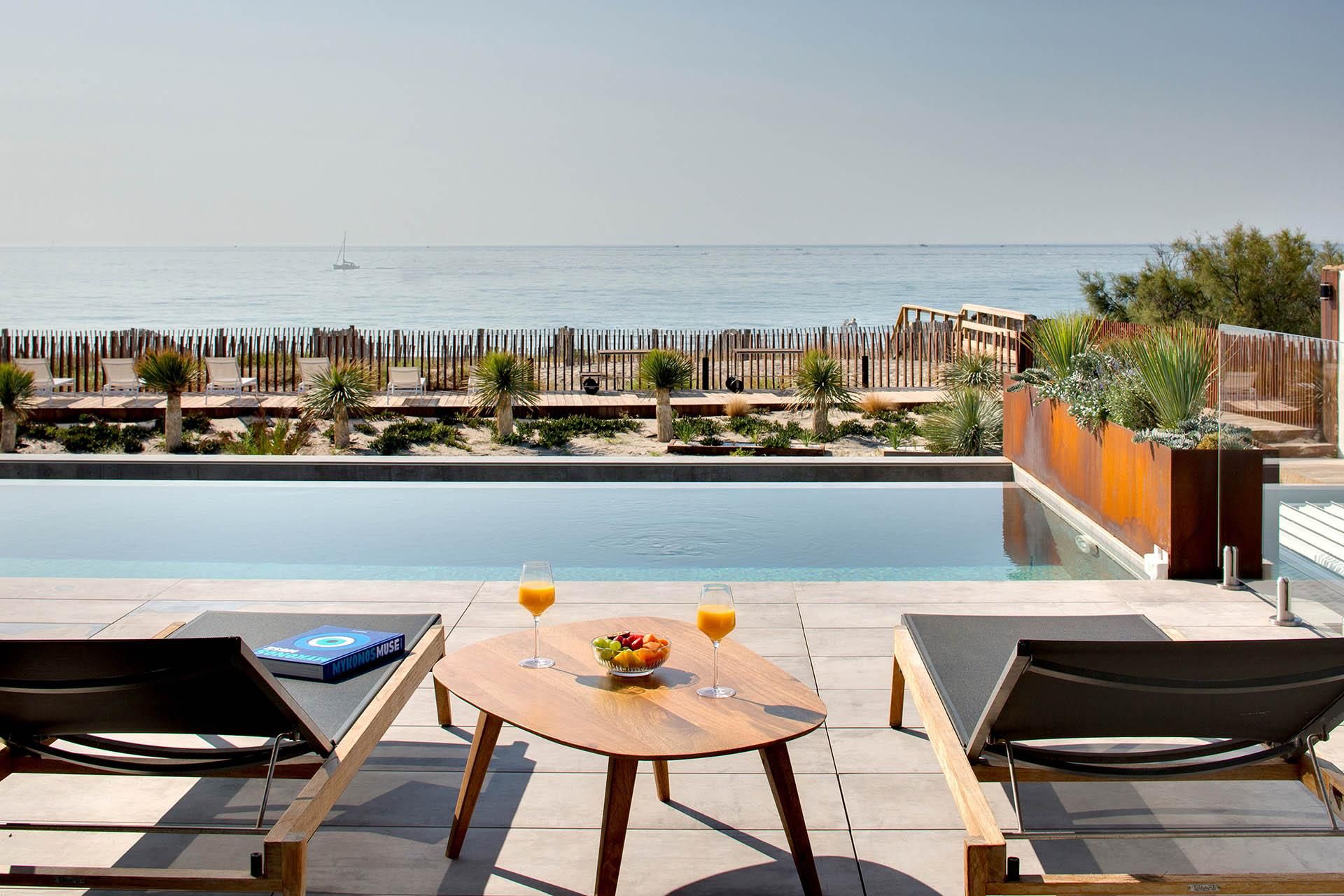 Zona de piscina con sillones reclinables, una mesa con frutas y bebidas, y vista al mar.