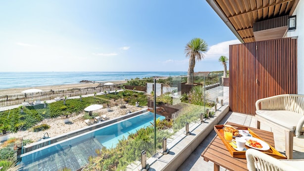 A poolside area with a view of the beach and ocean, a wooden deck, and a table with breakfast items. - Villa Miramar (Frontignan)